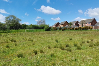 A football field which has been left to grow wild with houses in the distance