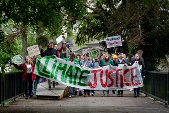 Young people marching for climate change holding placards and a large banner that reads 'climate justice'