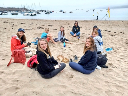 People sat on a beach in a circle whilst smiling at the camera