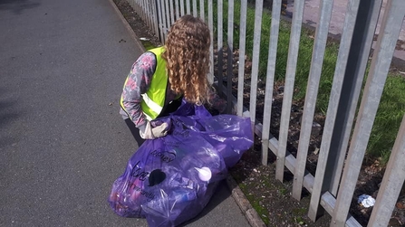 A young woman with curly hair wearing a high vis jacket is litter picking