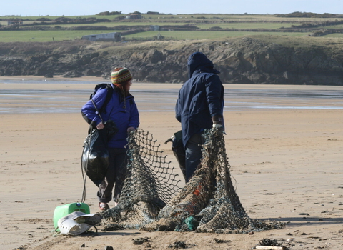 Two people drag marine litter on a beach