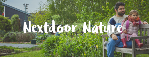 A father and daughter sit on a bench in a community garden, with a tree and bushes around them. The words 'Nextdoor Nature' appear overlaid