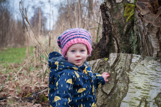 Poppy the toddler stands next to a tree stump