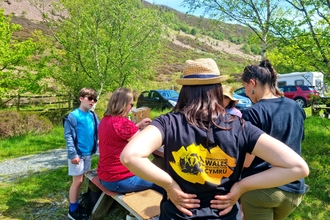 A woman wearing a Stand for Nature Wales branded tshirt with her back to the camera. There are children and adults doing crafts in the background.