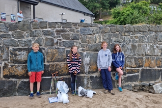 4 children lean against a wall with litter picking equipment nearby