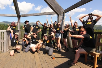 A photo of 15 people all wearing black tshirts with Stand for Nature Wales branding doing silly poses in a bird observatory