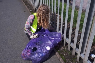 A young woman with curly hair wearing a high vis jacket is litter picking