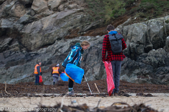 Two people litter picking on a beach, holding litter bags and litter pickers
