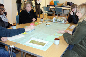A group of people sit around a table with a large piece of paper discussing ideas