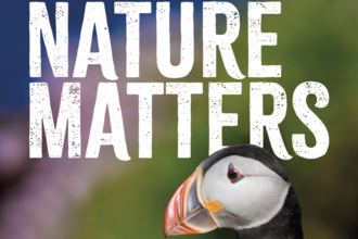 Poster from the Wildlife Trusts Wales with the text “Nature matters” in large white letters, featuring a close-up of a puffin against a softly blurred, colourful background, with the organisation’s logo in the top corner.