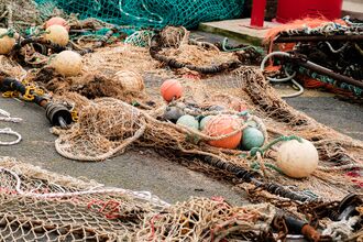 Fishing nets, ropes, chains and floats piled on a harbour quayside. The tangled fishing gear is spread across the ground, showing the equipment used in commercial fishing operations.