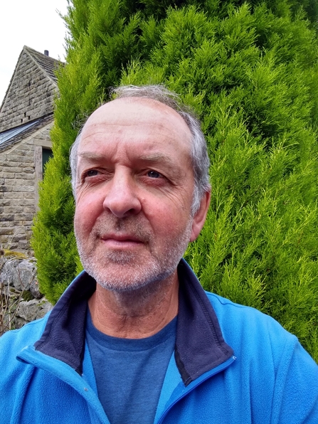 Photo of Tim Birch wearing blue jumper and stood in front of a tree