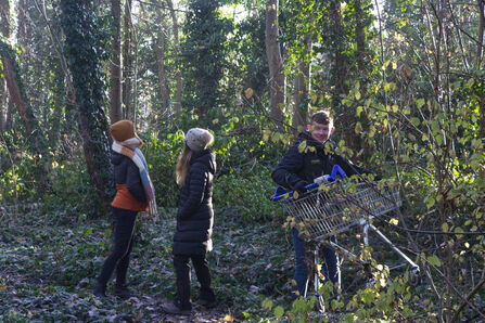 Volunteers removing a shopping trolly from wooded area. 