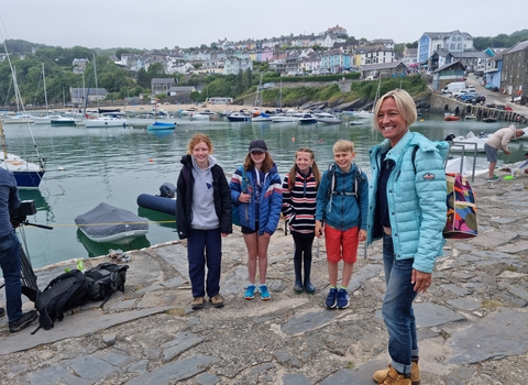 4 children stand with a woman on a pier with a coastal village in the background