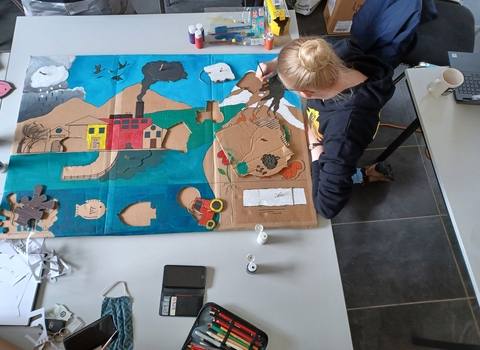 A young woman painting a climate change diagram on cardboard, photo is taken from above