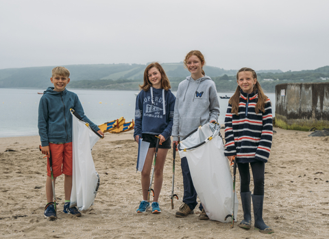 An image of 4 children smiling at the camera on a beach holding litter picking equipment