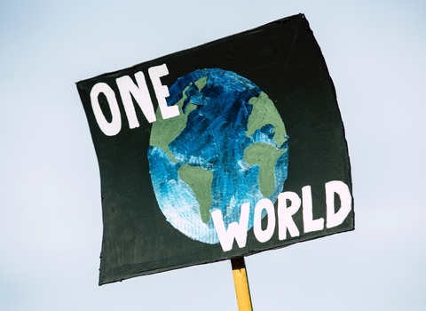 A placard which reads 'One World' with an image of the Earth on a black background