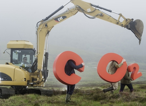 A digger and 3 people holding huge CO2 letters on a peatbog