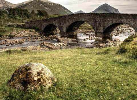 A arched bridge over a river with mountains in the background